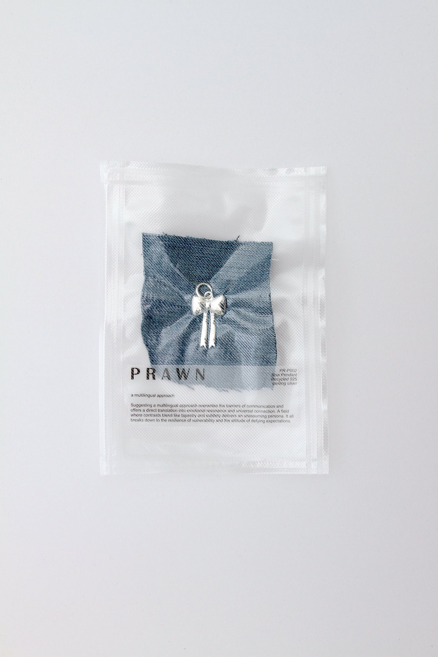 Large, puffy bow charm pendant lying on denim in vacuum packaging on a light gray background