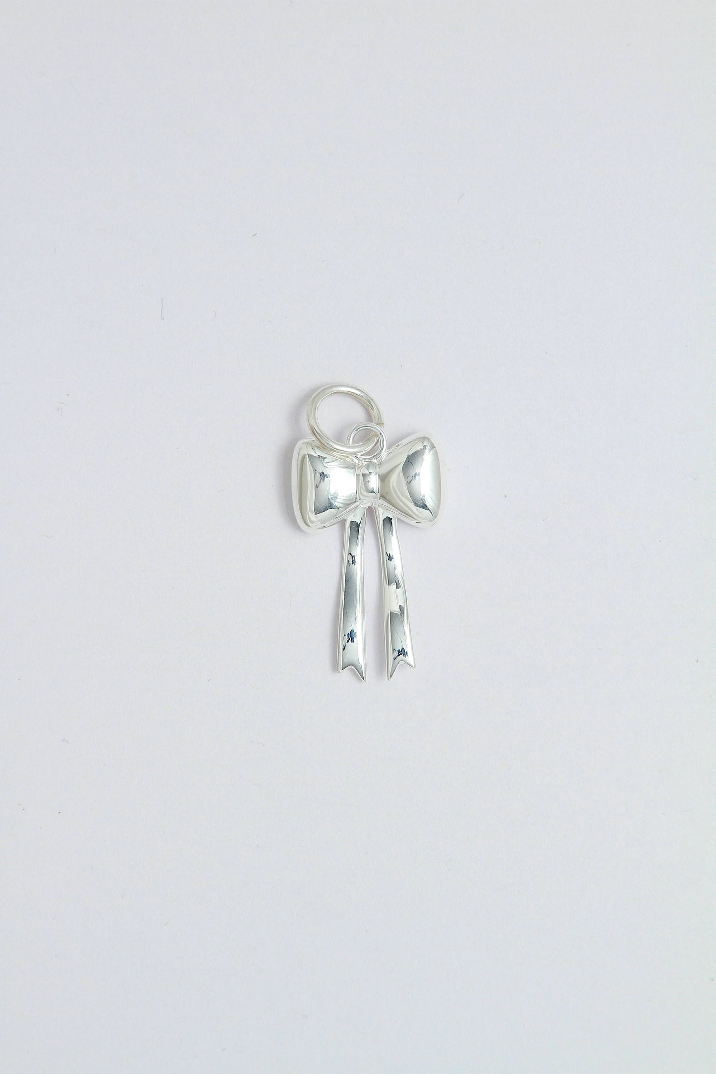 Silver bow-shaped charm pendant that can be attached on a necklace or a hoop earring