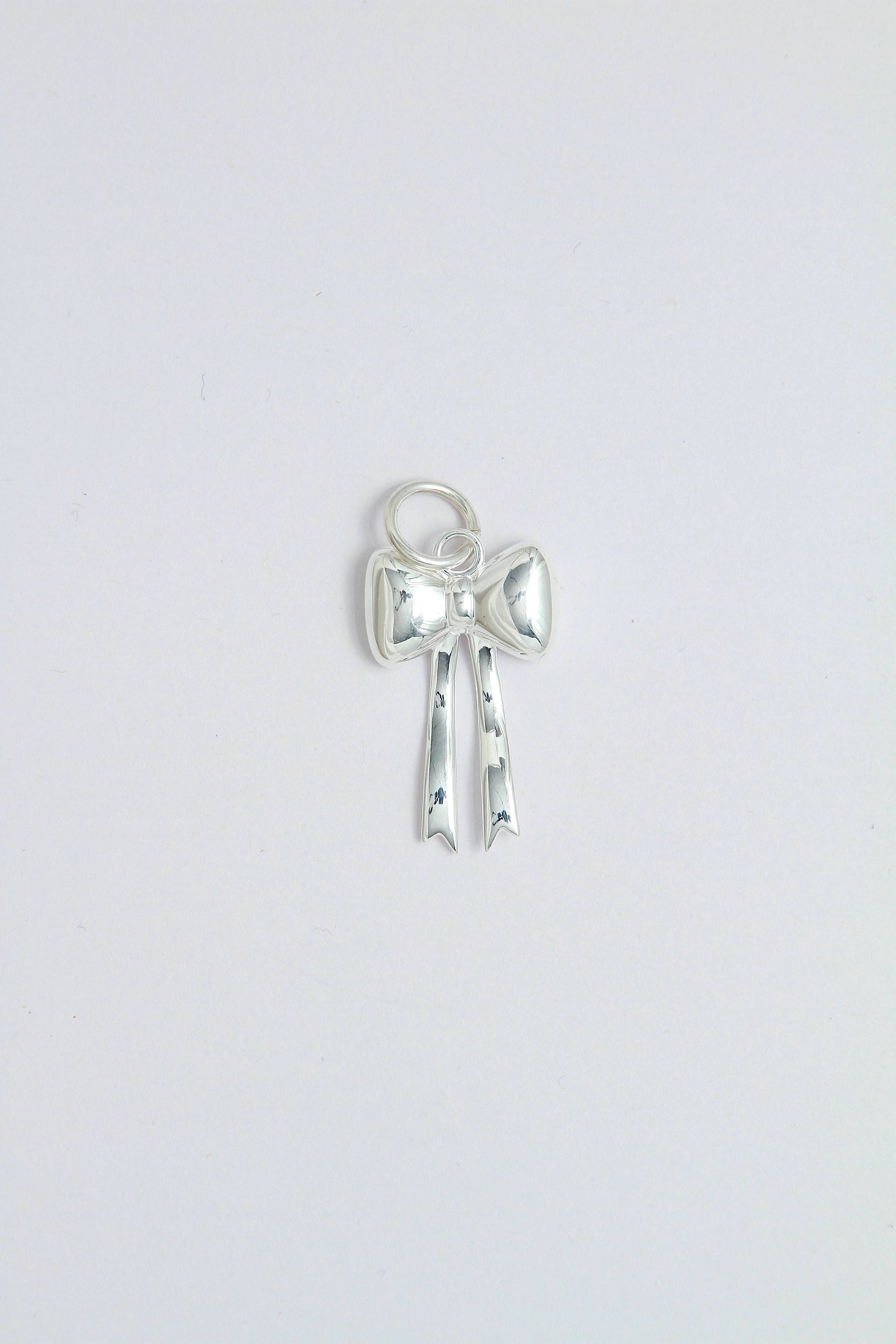 Silver bow-shaped charm pendant that can be attached on a necklace or a hoop earring