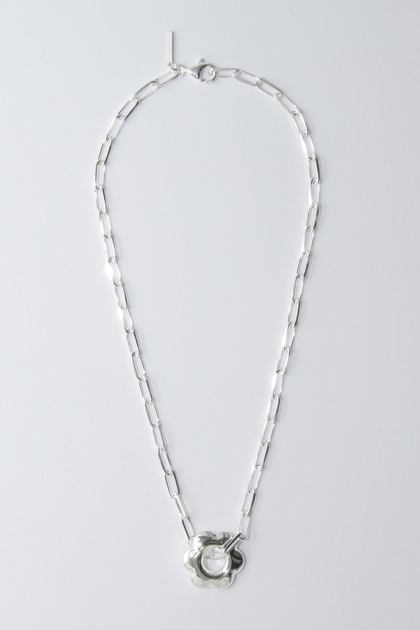 Silver necklace with a puffy, flower pendant on a light gray background
