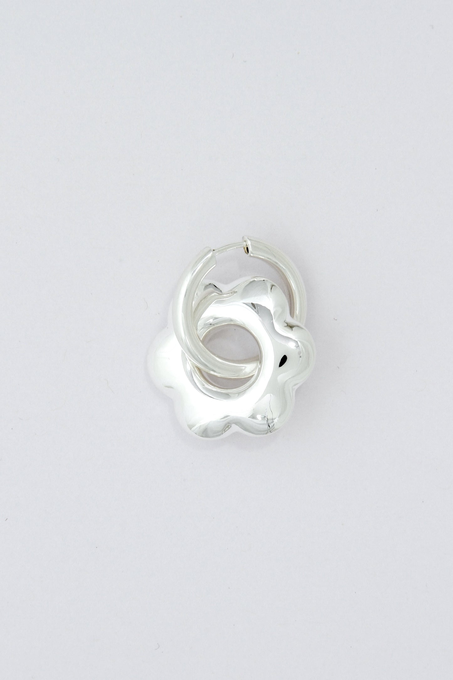 Large, puffy flower, silver hoop earring on a light gray background