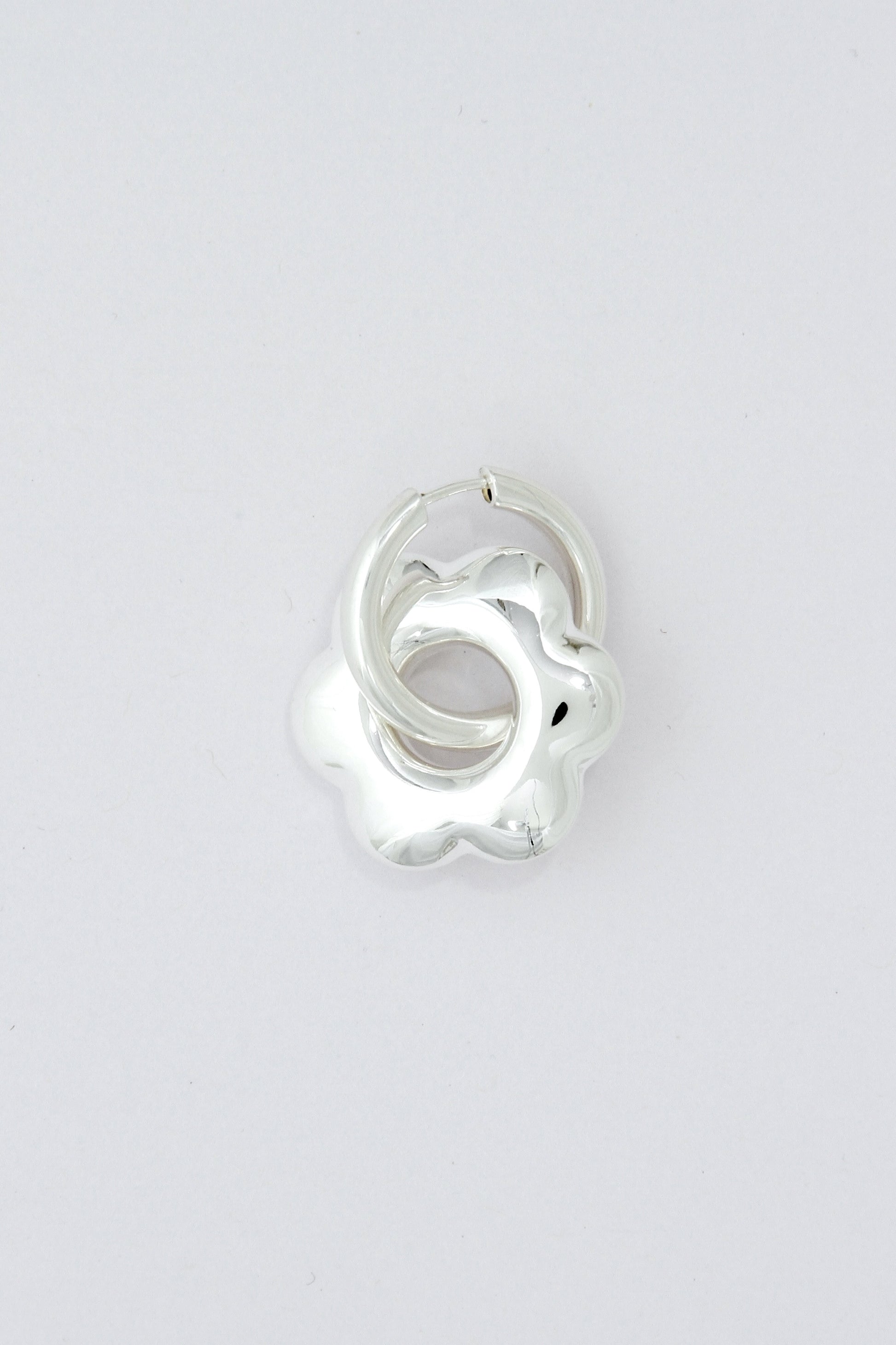 Large, puffy flower, silver hoop earring on a light gray background