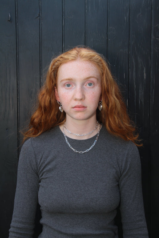 Woman wearing a chunky silver necklace and heart hoop earrings