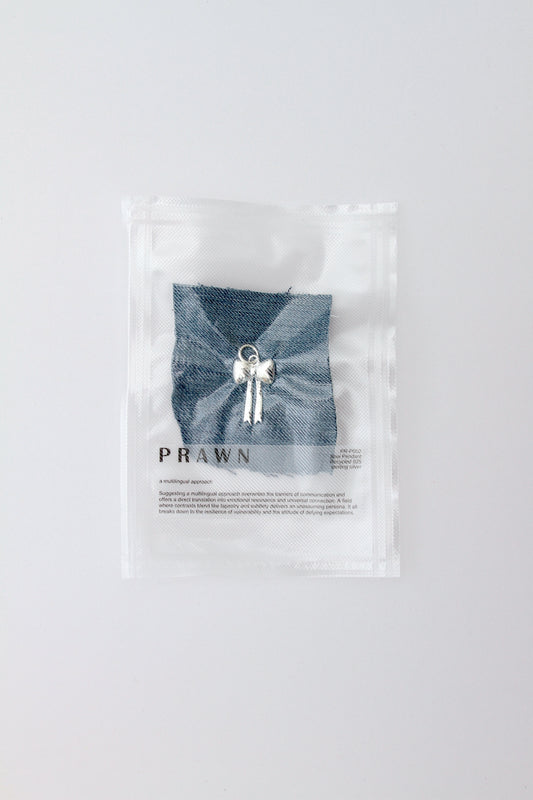 Large, puffy bow charm pendant lying on denim in vacuum packaging on a light gray background