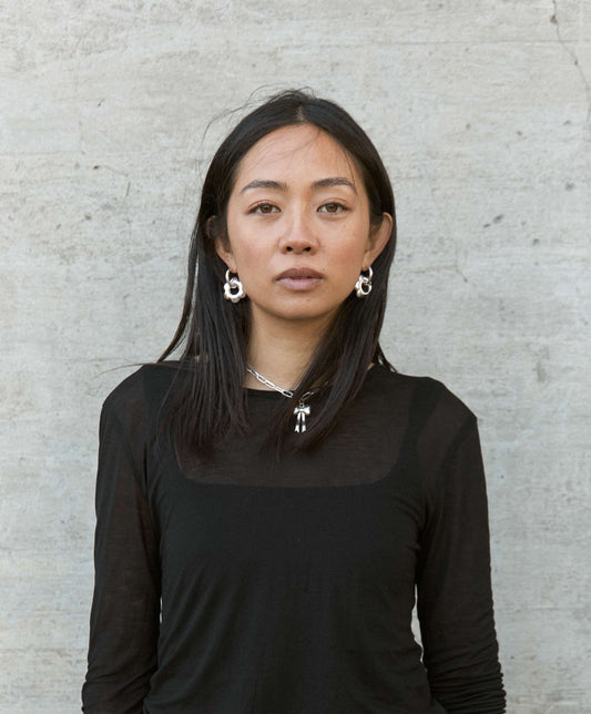 Woman wearing large, puffy flower, silver hoop earrings against a light gray concrete background